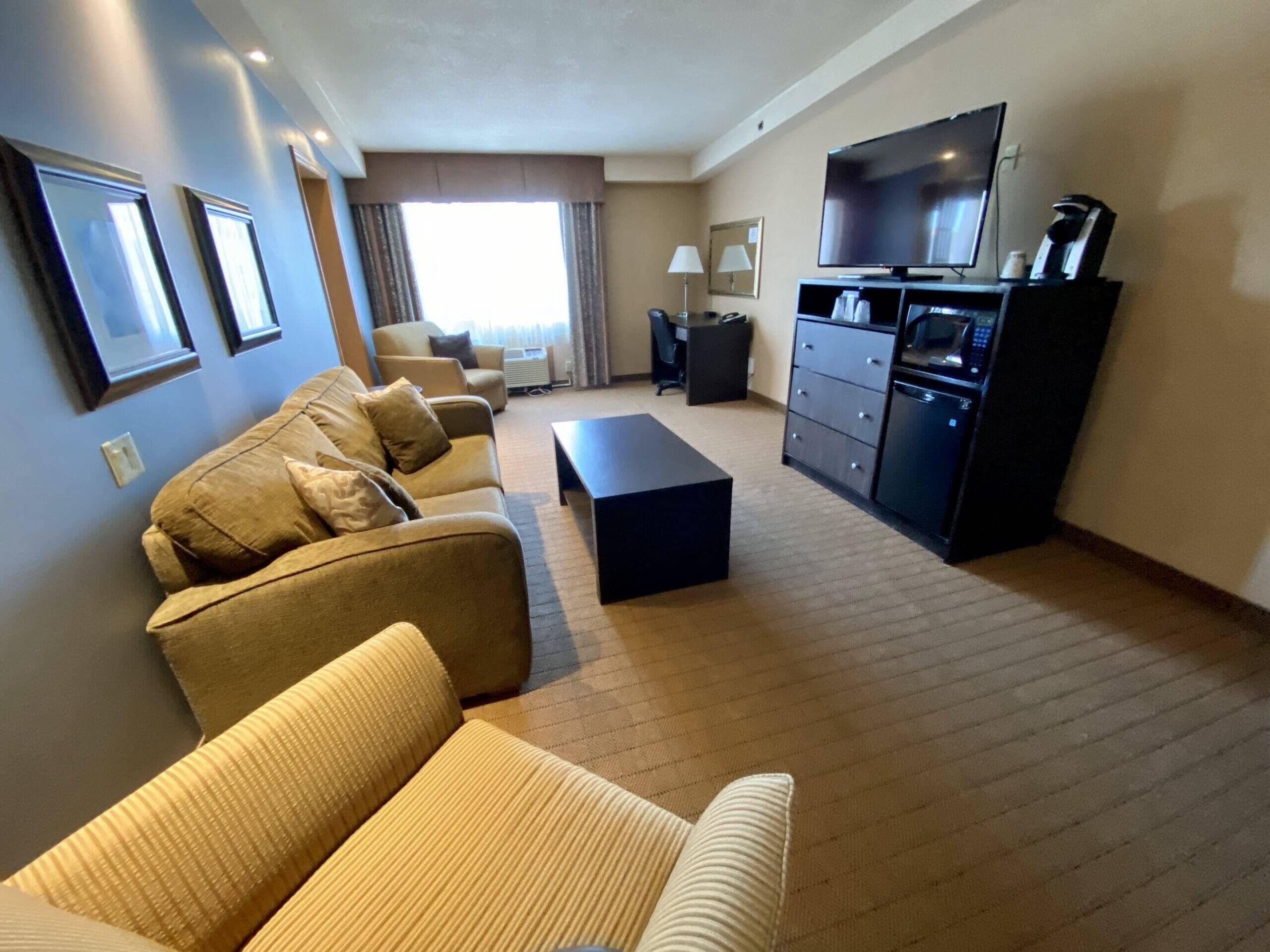 A living room with a sofa set, a coffee table, a TV, and a kitchenette area.