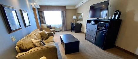 A living room with a sofa set, a coffee table, a TV, and a kitchenette area.
