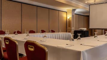 Un salón de conferencias con una larga mesa, sillas rojas y una pantalla para proyector.