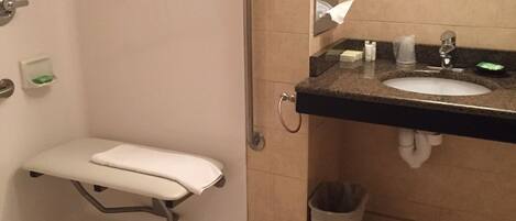 A small, private bathroom with a toilet, a handrail, a sink, and a trash can.