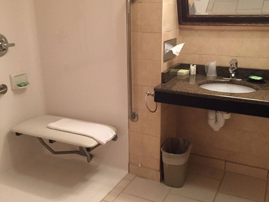 A small, private bathroom with a toilet, a handrail, a sink, and a trash can.