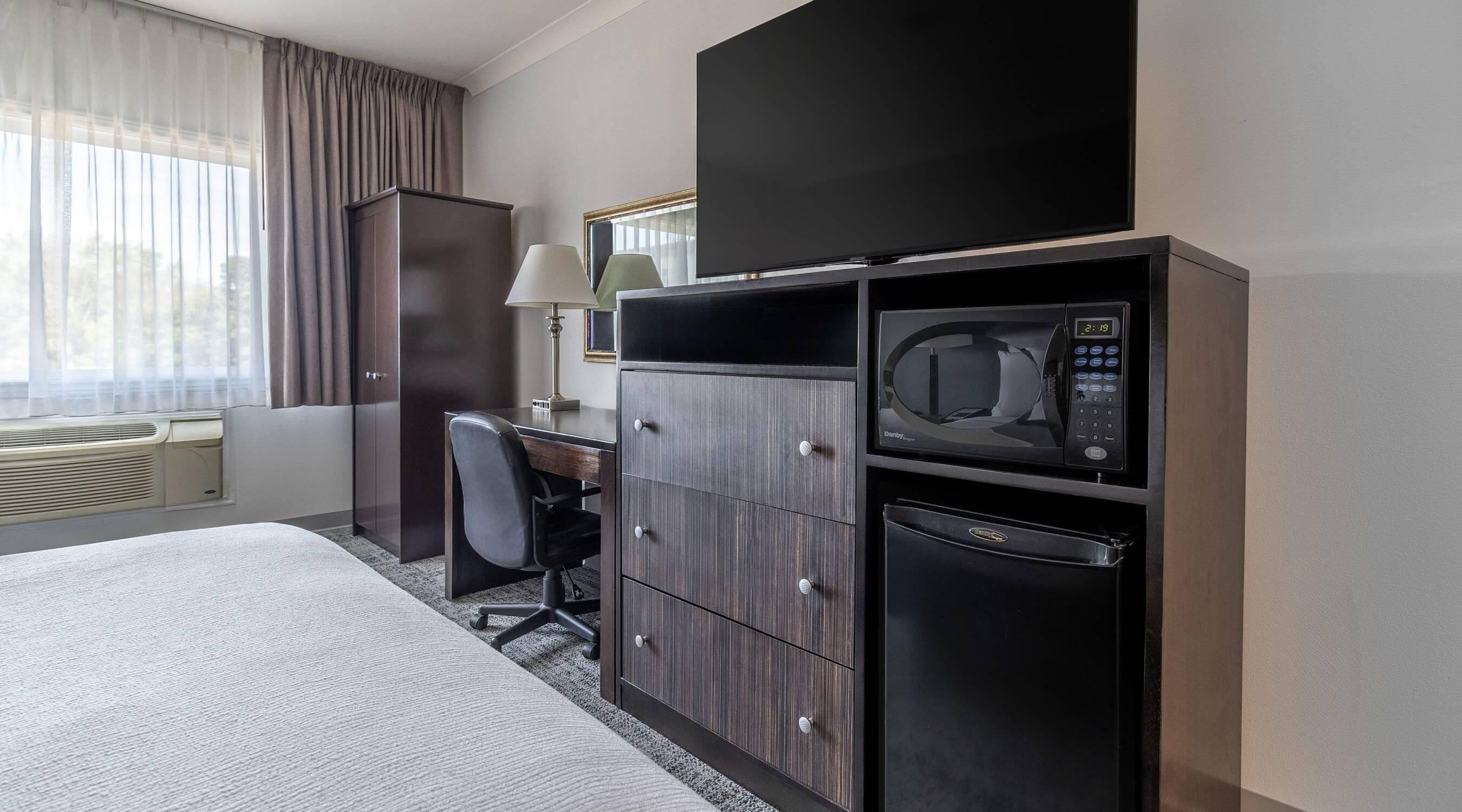 A hotel room with a bed, desk, chair, TV, microwave, and mini-fridge.