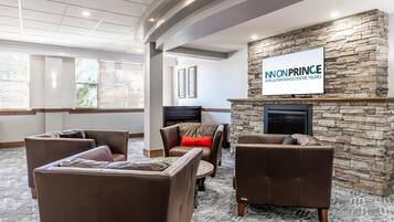 A lobby with brown leather sofas, a stone fireplace, and a television displaying 'INONPRINCE HOTEL & CONFERENCE CENTRE TRURO.'