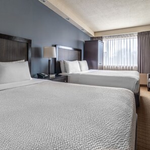 A hotel room with two beds, a nightstand with a lamp, a wardrobe, and a window with curtains. - Inn on Prince Hotel & Conference Centre, an Ascend Collection Hotel (Truro)