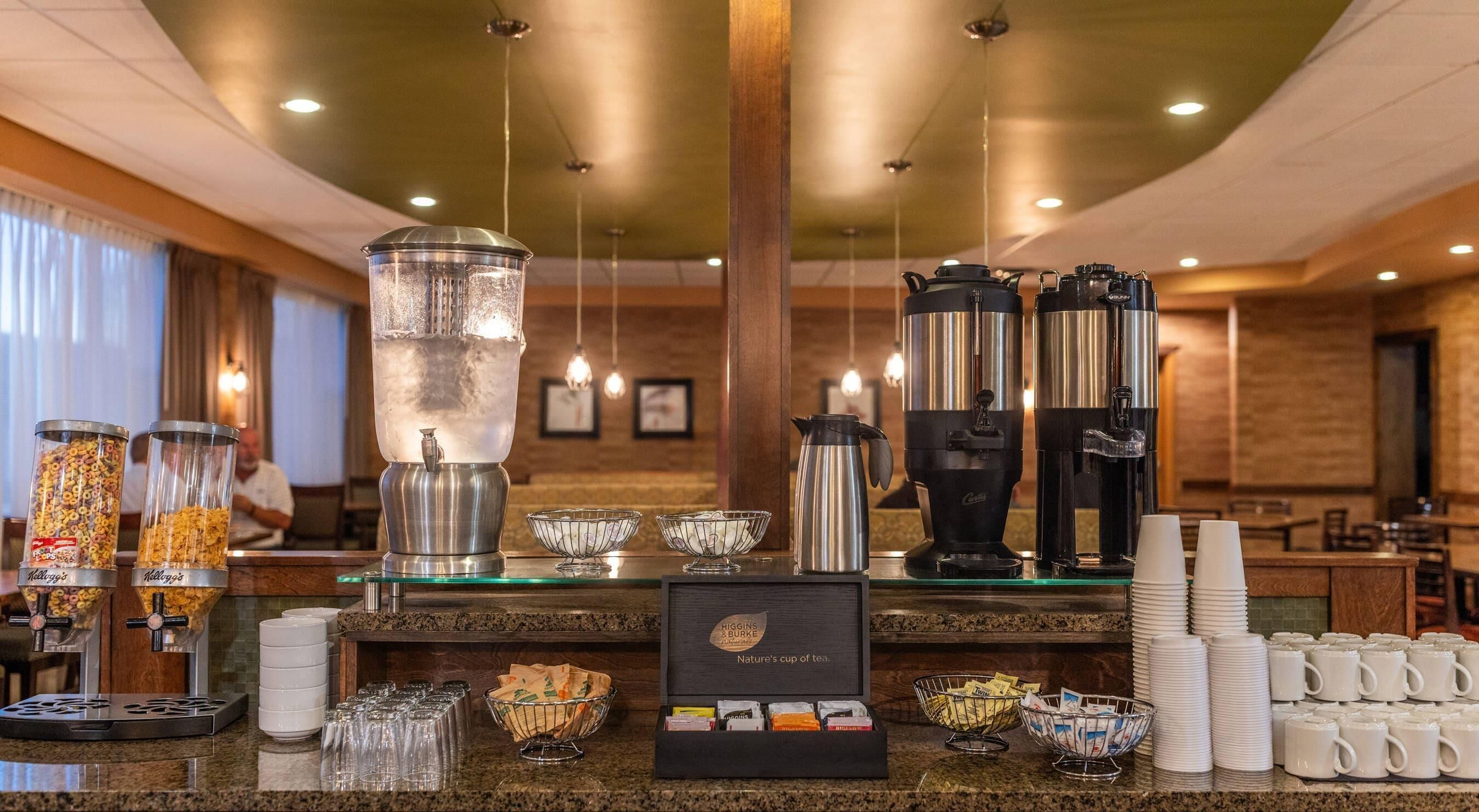 A hotel breakfast bar with a coffee machine, tea kettle, cereal dispensers, and a tea display.