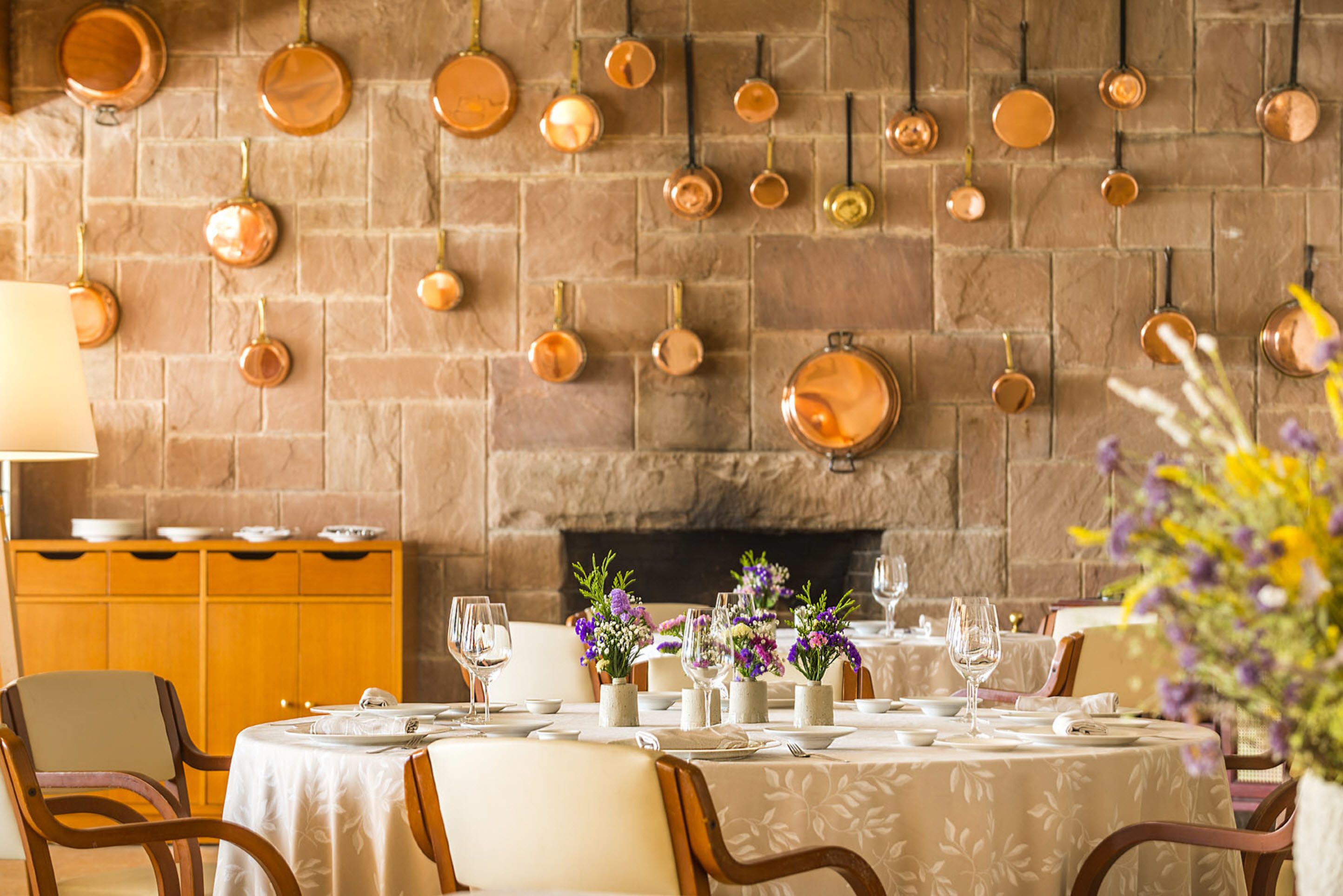 A dining area with a stone wall, hanging copper pots, and a table set for a meal.