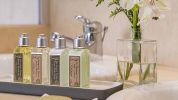Un tocador de baño con cinco productos de L'OCCITANE, un florero con flores blancas y una pastilla de jabón.
