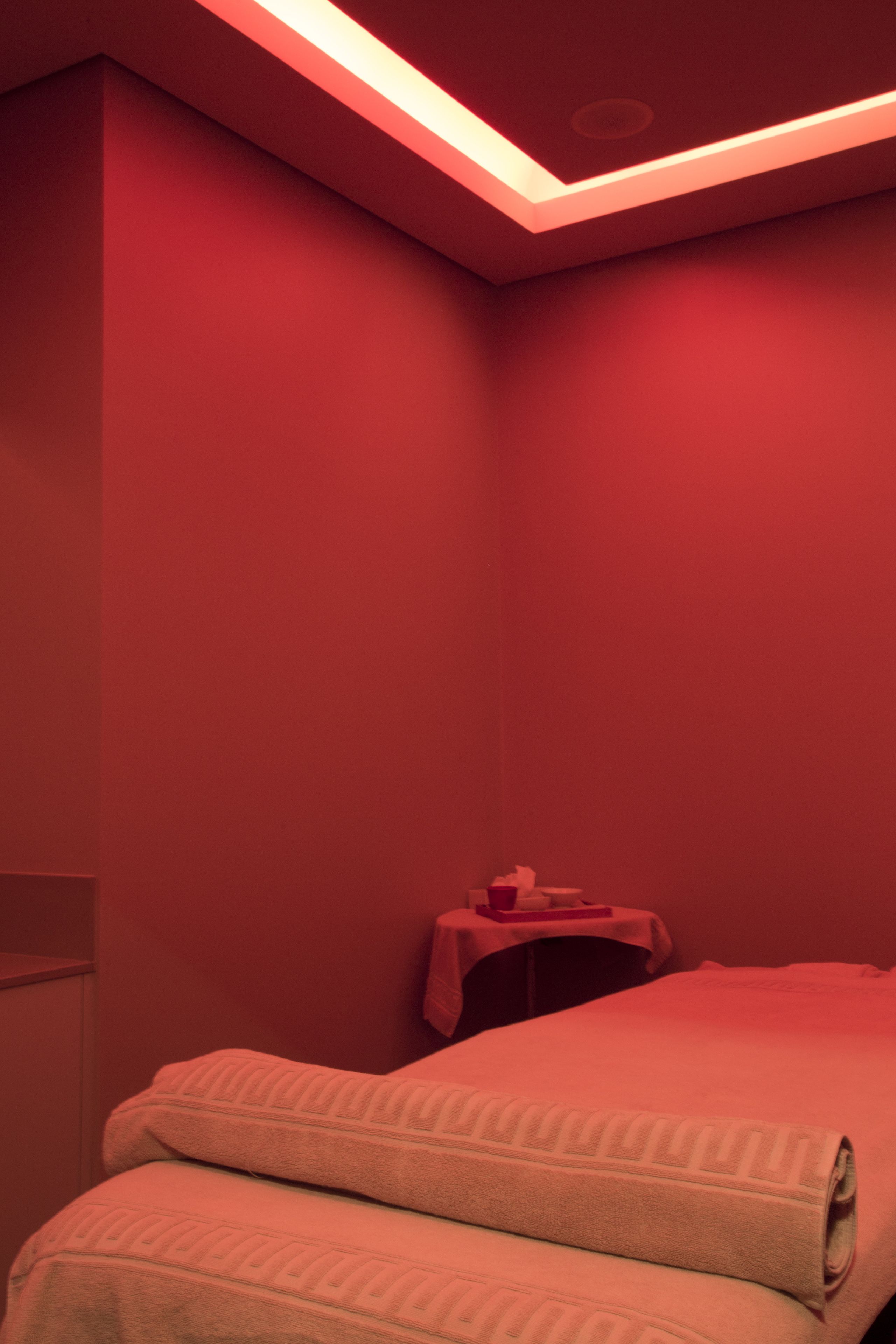 Une pièce avec un lit, une petite table recouverte d’une nappe rouge et un luminaire au plafond.