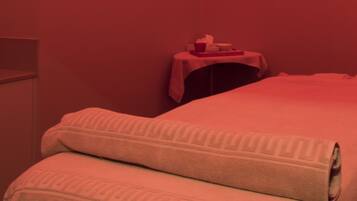Una habitación con una cama, una mesita con un mantel rojo y una lámpara en el techo.