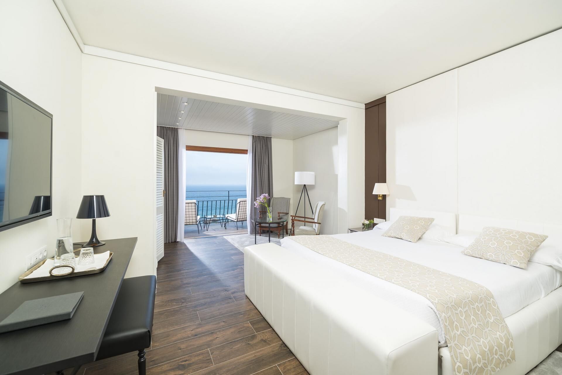 Une chambre d’hôtel avec un grand lit, un bureau avec une lampe, une chaise et une vue sur la mer.