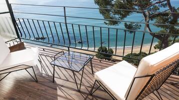 A balcony with a view of the sea, wooden flooring, and two white chairs.