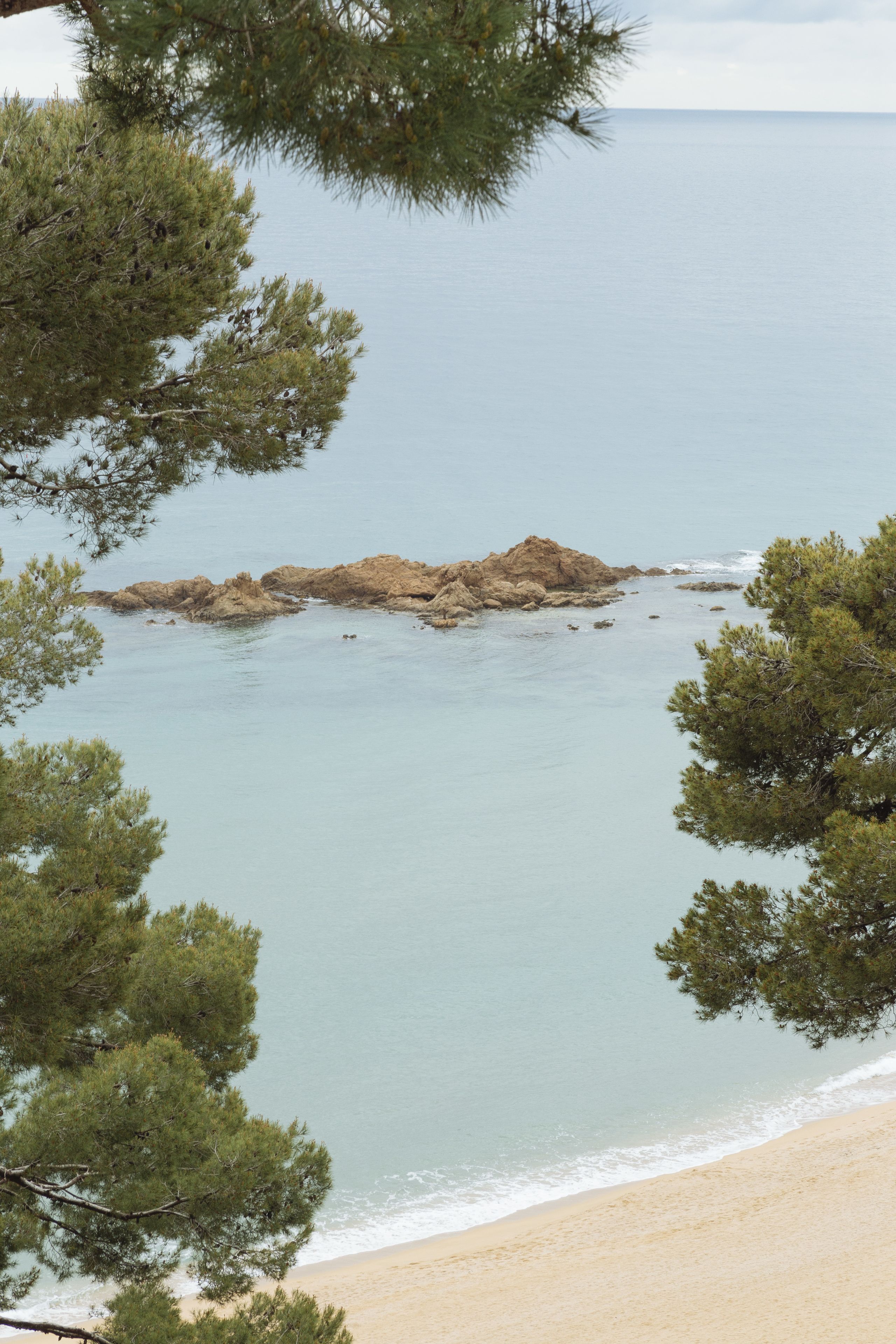 A coastal scene with a sandy beach, calm sea, and rocky outcrops.
