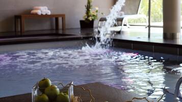 Ein Wellnessbereich mit Whirlpool, einem Tisch mit Äpfeln und einem Korb sowie ein Liegestuhl am Fenster.