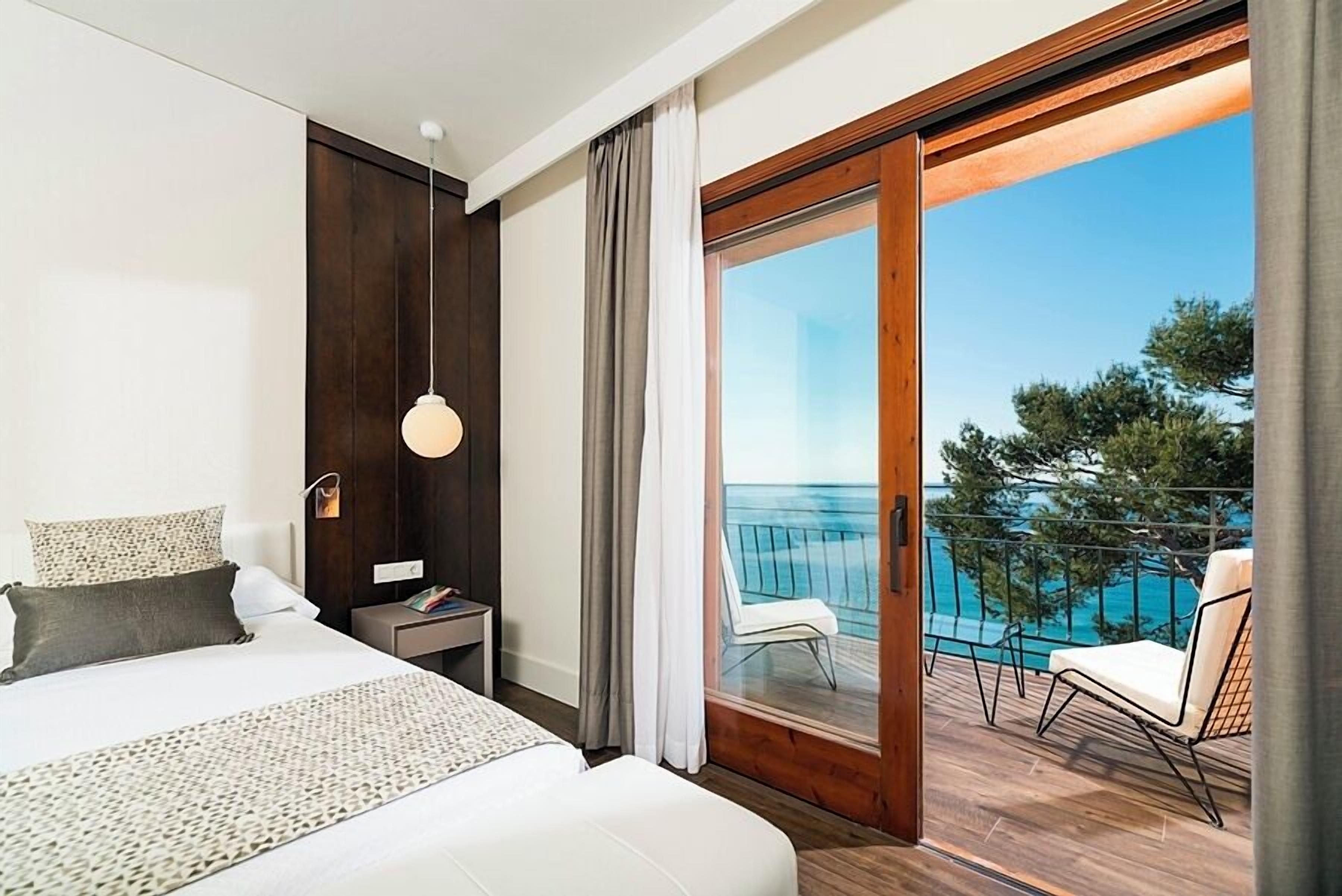 Hotelkamer met een bed, nachtkastje, lamp en een balkon met uitzicht op zee.
