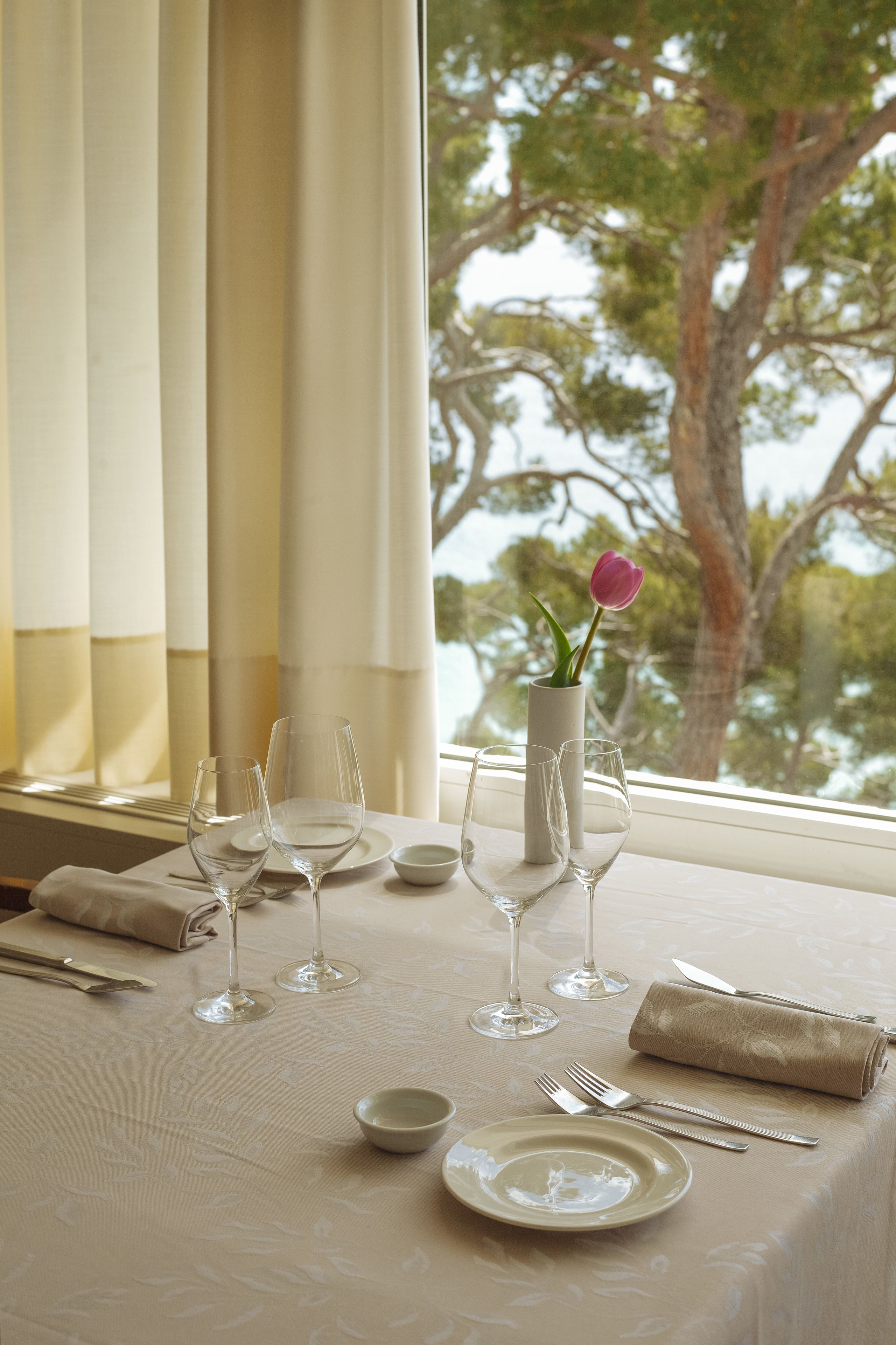 A table set for dining with a vase of flowers, clear glasses, and cutlery.