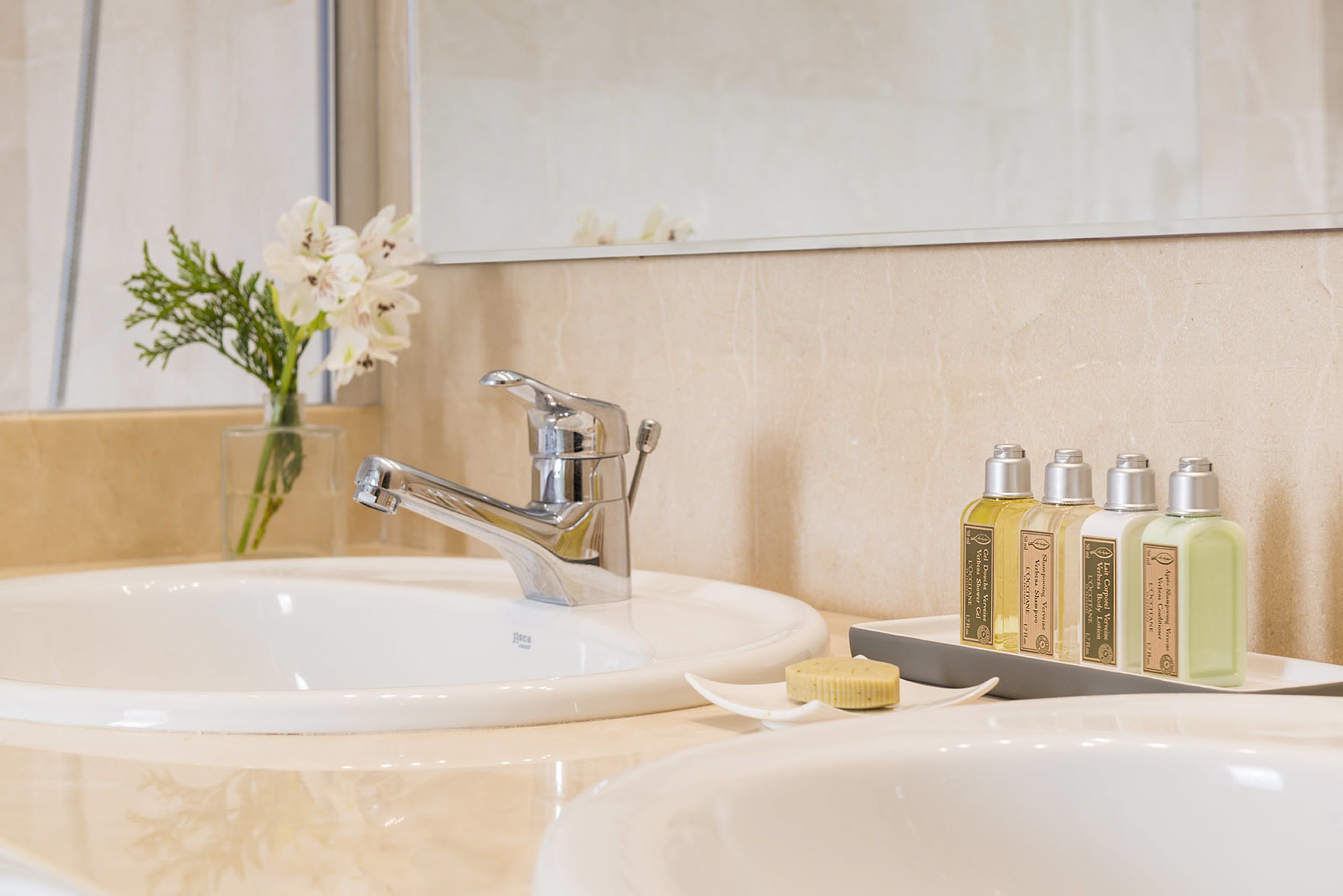 A bathroom with two sinks, a mirror, and a row of toiletries.