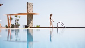 Una persona che cammina vicino a una piscina con una struttura in pietra e palme.