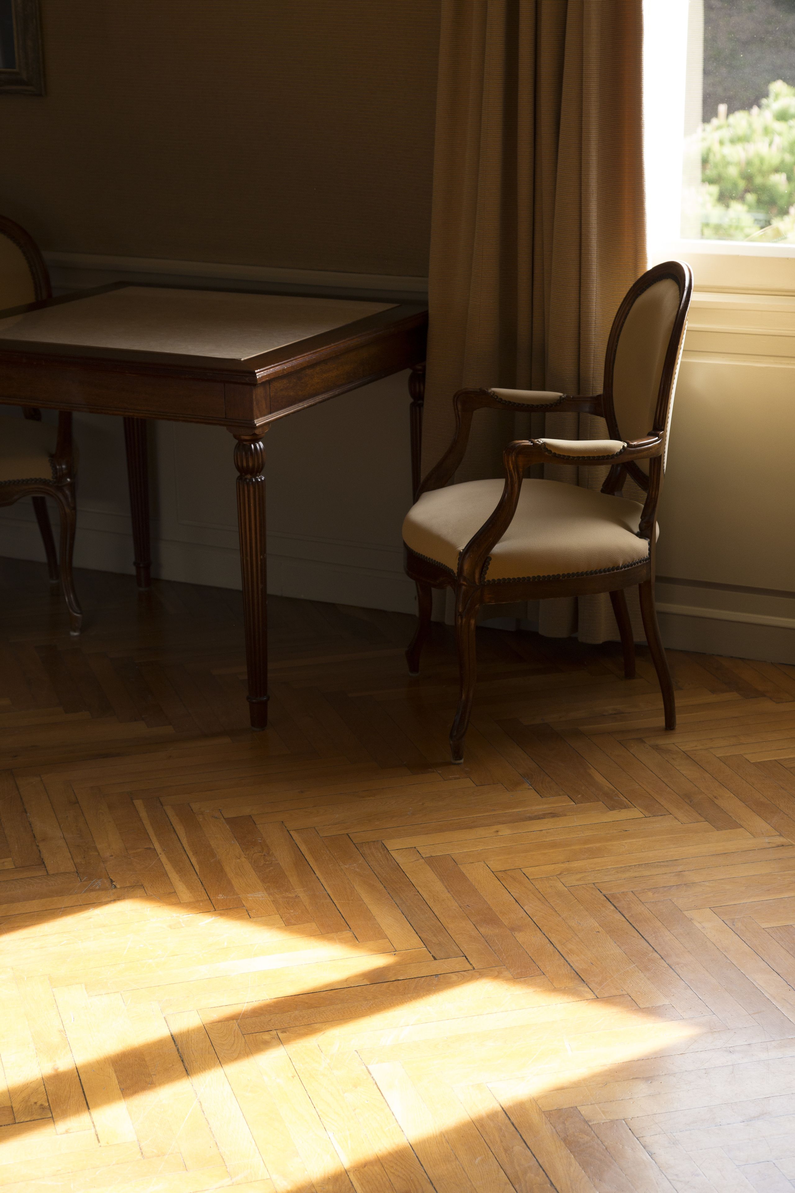 A room with a wooden floor, a dining table, and a chair near a window with curtains.