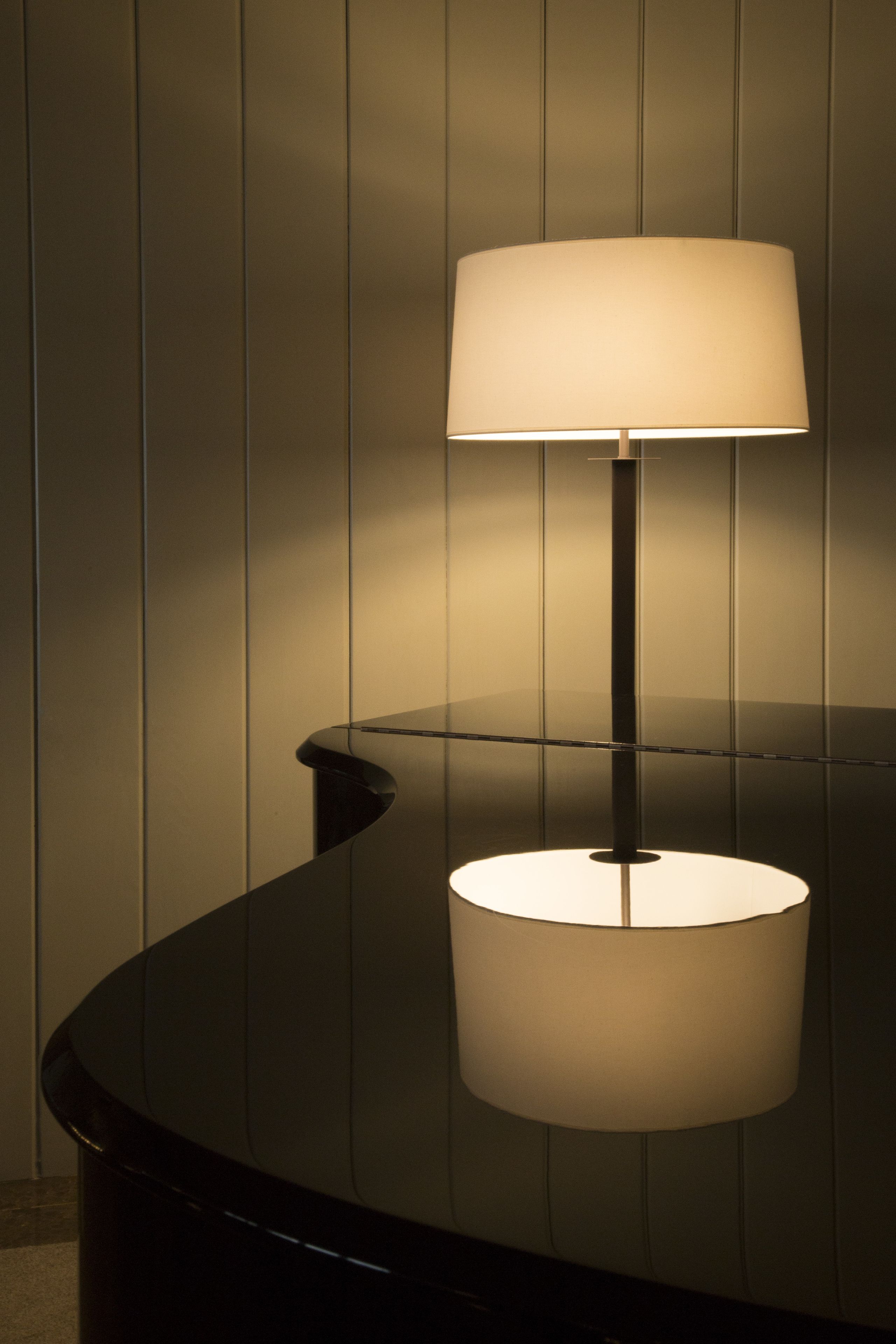 Een lamp op een glanzende zwarte tafel, achter een houten wand.