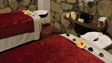 Relax in a serene spa room with two massage beds, a shelf with candles and a potted plant.