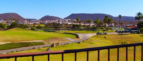 Un parcours de golf offrant une vue sur une ville et, au loin, sur des montagnes.
