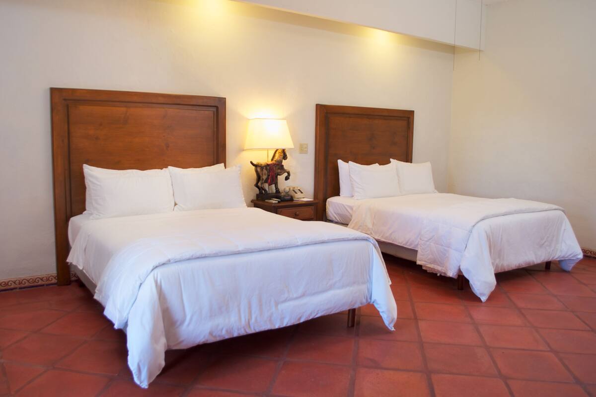 A hotel room with two single beds, a nightstand with a lamp, and a decorative item on the nightstand.