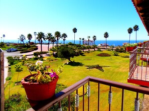 A balcony with a view of a well-maintained garden, palm trees, and a building in the background. - Hacienda Bajamar Golf Resort (Salsipuedes)