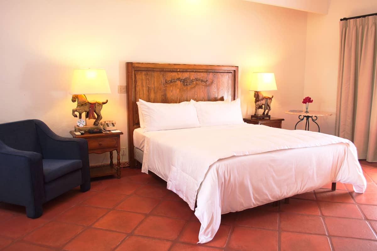 A hotel room with a large bed, two bedside tables with lamps, a chair, and a small table with a vase of flowers.