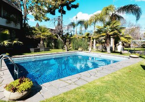Una piscina con borde de piedra, rodeada de césped y palmeras.