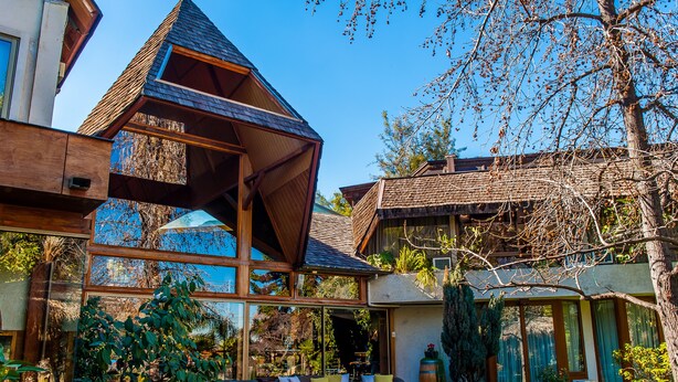 A modern house with a unique triangular roof, large glass windows, and a well-maintained garden.