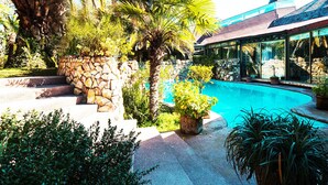 A pool area with a stone wall, palm trees, and a building with a blue roof.