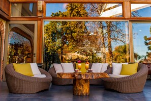 A modern outdoor seating area with wicker furniture and a central wooden table, overlooking a lush garden. - Manquehue Las Condes Hotel (Santiago)