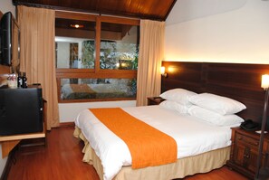 Una habitación de hotel con cama, televisión, mesita de noche y ventana con cortinas.