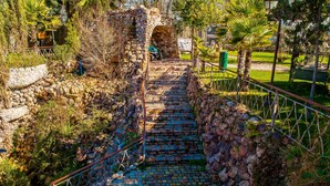 A stone pathway leading to a stone archway, surrounded by greenery and a metal railing.