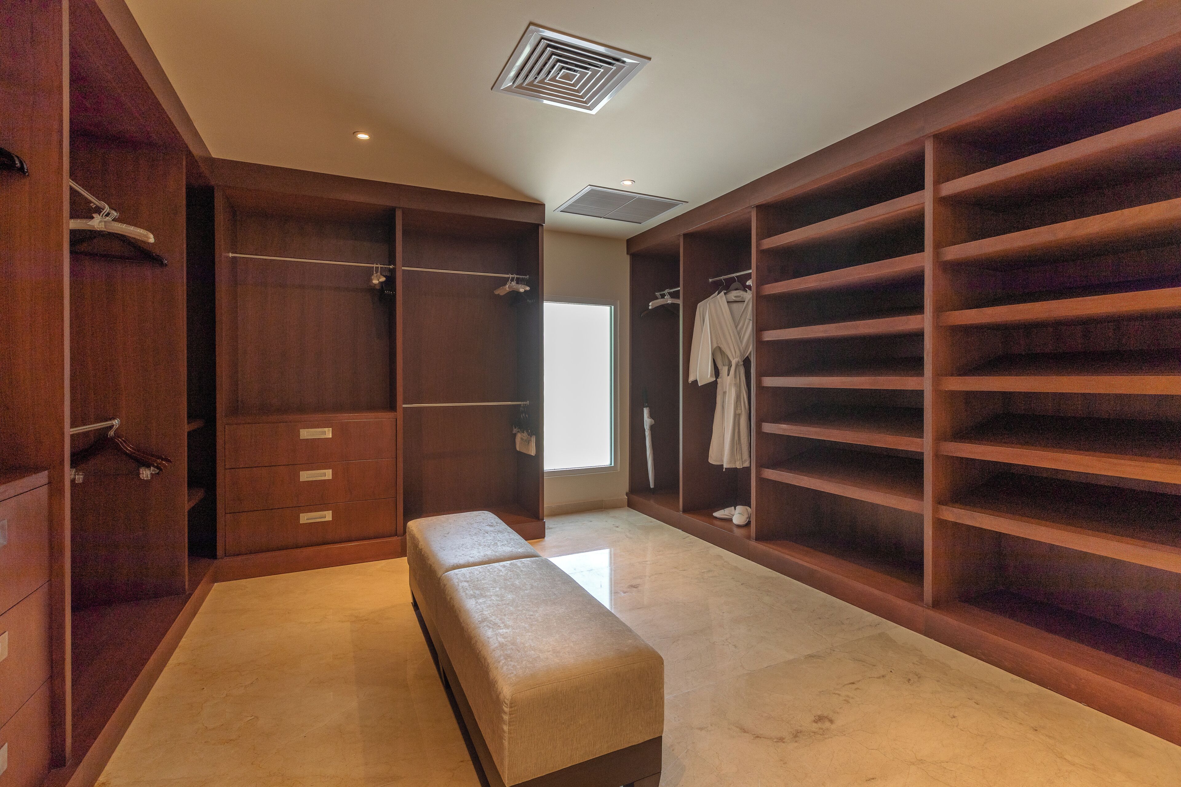 A walk-in closet with wooden shelving, a bench, and a large mirror.