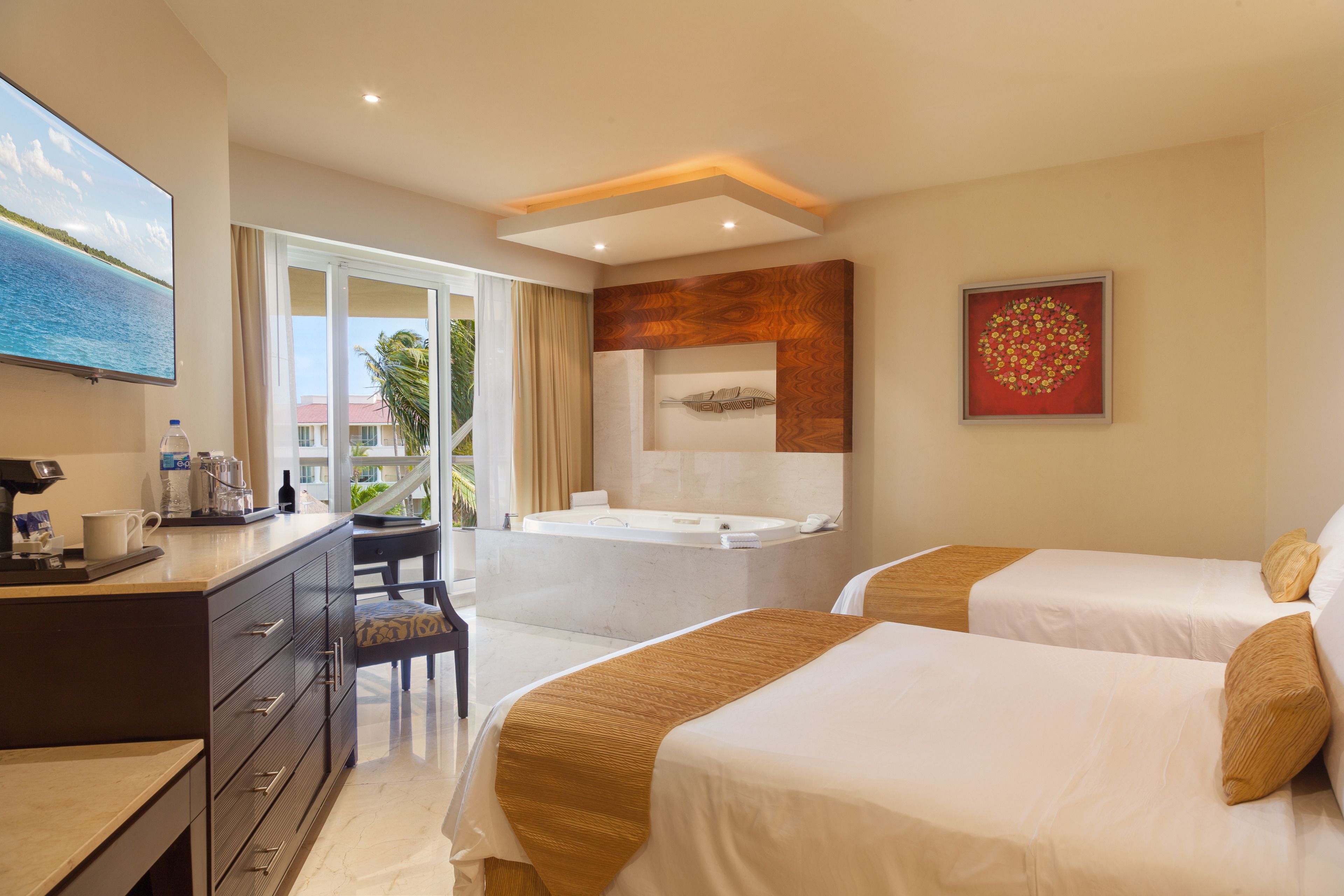A hotel room with two beds, a desk, a coffee maker, a TV, a bathtub, and a large window with a view of palm trees.