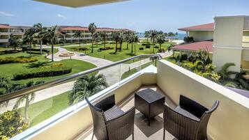 Ein Balkon mit Rattanmöbeln, freier Blick auf die angelegten Grünflächen eines Resorts und ein weiter Blick aufs Meer.