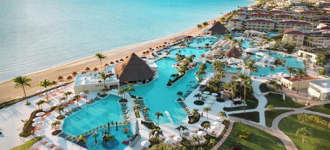 Un resort con varias piscinas, una playa y palmeras.