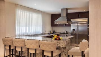 A modern kitchen with a central island, bar stools, stainless steel appliances, and a large window with sheer curtains.