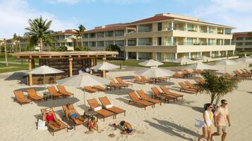 Na praia, areia branca, espreguiçadeiras, guarda-sóis