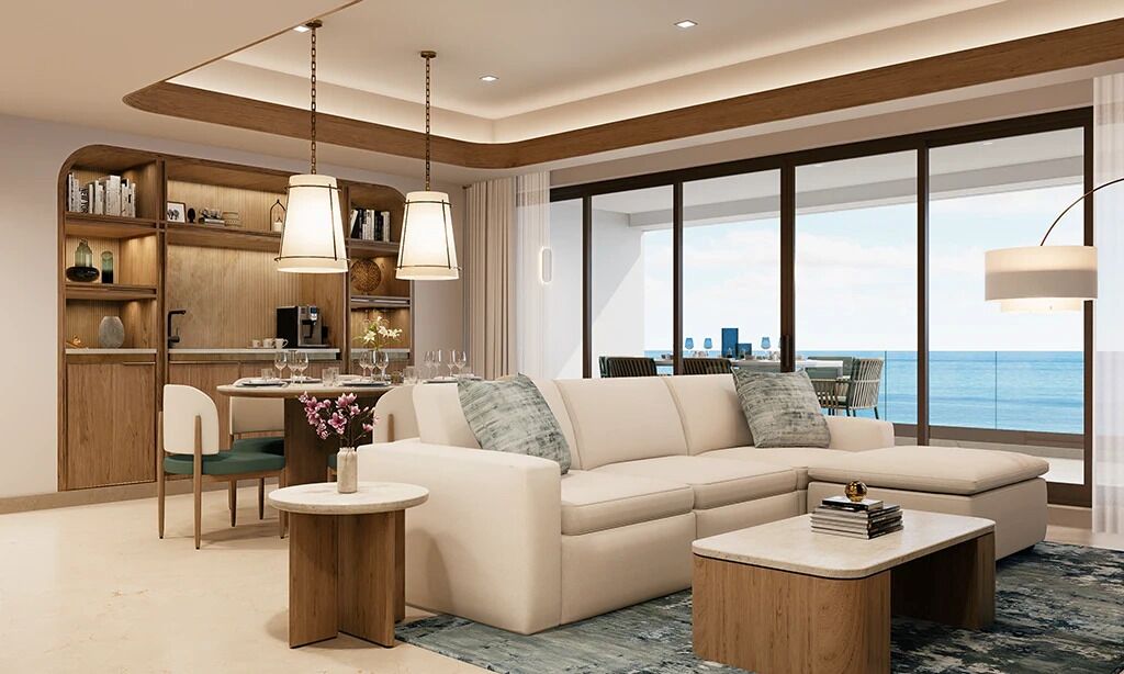 A modern living room with a sofa, coffee table, and dining area, featuring a large window with a view of the sea.