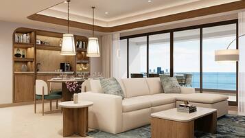 A modern living room with a sofa, coffee table, and dining area, featuring a large window with a view of the sea.