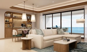 A modern living room with a sofa, coffee table, and dining area, featuring a large window with a view of the sea.