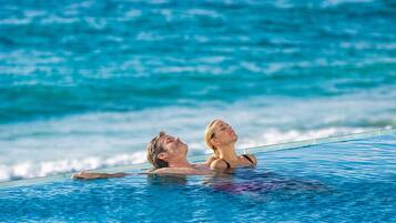 Ein Paar entspannt in einem klaren, blauen Infinity-Pool, mit Blick auf das Meer im Hintergrund.