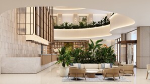 Eine moderne Lobby mit einer geschwungenen Treppe, einem Empfangsbereich und einer Sitzecke mit Pflanzen und Möbeln.