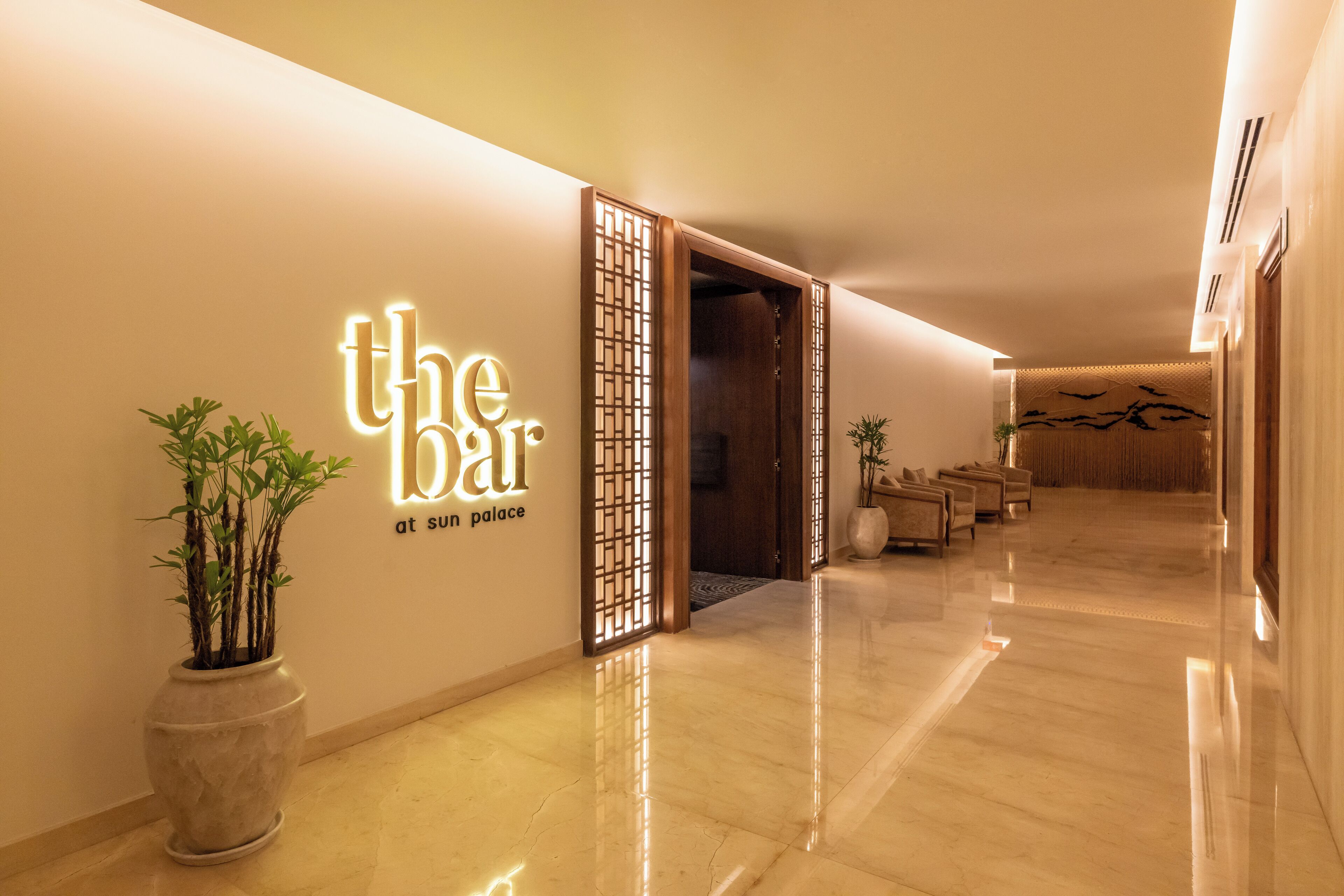 A hotel lobby with a polished marble floor, a reception desk, and a sign that reads "the bar at sun palace."