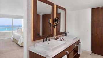 A modern bathroom with dual sinks, large mirrors, and a view of the ocean.