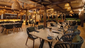An indoor restaurant with multiple dining tables and chairs, a bar area with shelves of bottles, and hanging wicker lamps. - Sun Palace Cancun - Adults Only - All-inclusive (Cancun)