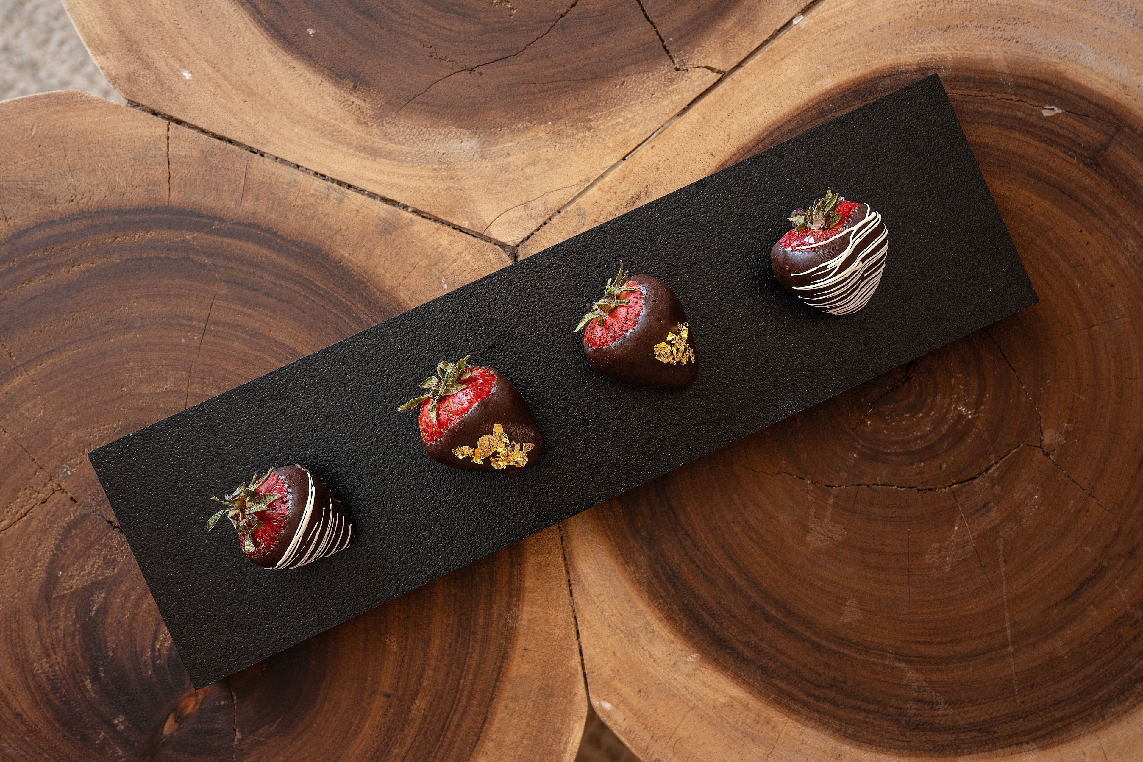 A chocolate-covered strawberry on a black slate, placed on a wooden surface.