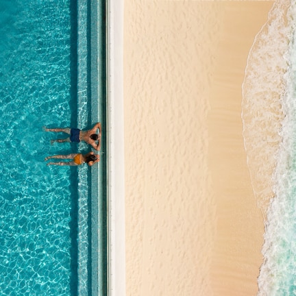 An aerial view of a beach with clear blue water and a sandy shore.